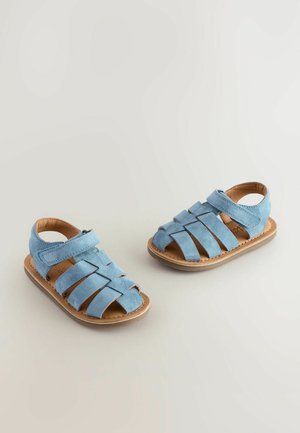 Sandale din suede de culoare albastru deschis, cu un design împletit, vârful deschis, curea reglabilă și talpă din cauciuc bej. Ideale pentru vreme caldă.