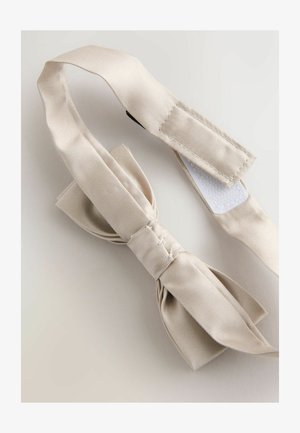 Bež mašna od tkanine s teksturiranim završetkom, s čvorićem u sredini i podesivim remenom s čičak zatvaračem.