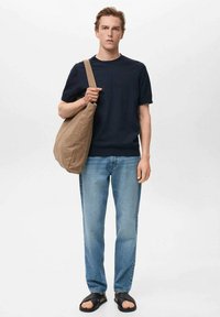 Marineblauw T-shirt met korte mouwen, lichtblauwe jeans, zwarte sandalen en een beige canvas schoudertas. Eenvoudige, relaxte pasvorm met een natuurlijke textuur.
