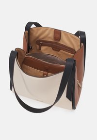 Strukturalna torebka z kremowo-beżowym przodem, brązowymi akcentami oraz czarnymi skórzanymi paskami. Wewnątrz znajduje się kilka przegródek i zamków.