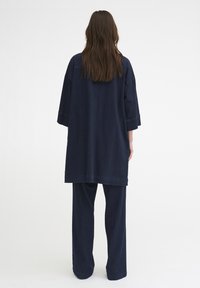 Námořnické modré oversized tunika a odpovídající široké kalhoty, vyrobené z tkaniny podobné džínsům, s uvolněným střihem a ohrnutými manžetami.