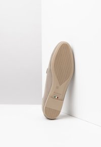 Beige Wildledersohle mit einer strukturierten Gummigriff, versehen mit einem Etikett, das "NeroGiardini" liest, und einem kleinen italienischen Flaggenemblem.