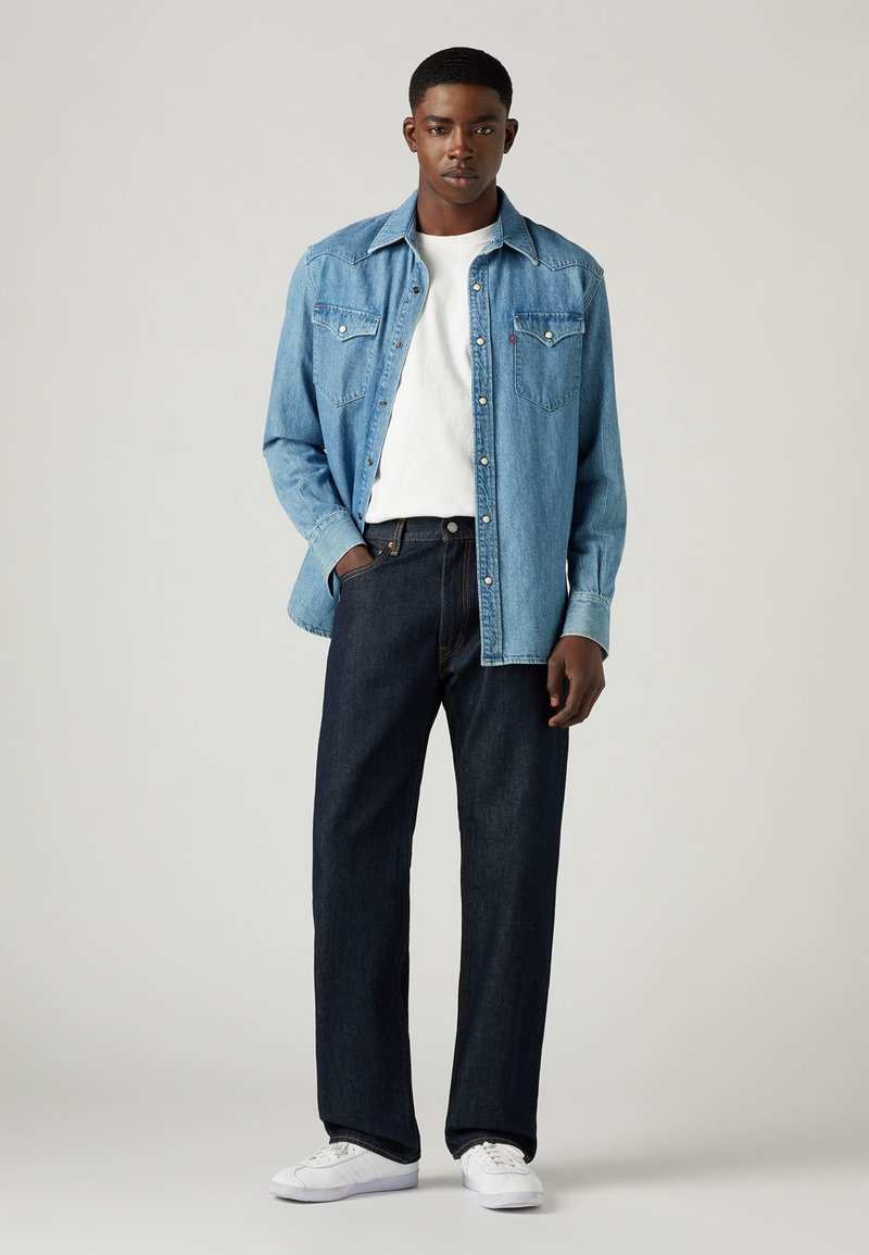 Helles blaues Denimhemd, weißes Rundhals-T-Shirt, dunkelblaue Jeans und weiße Sneaker; gerade Passform, klassisches westliches Design mit Knopfdetails.