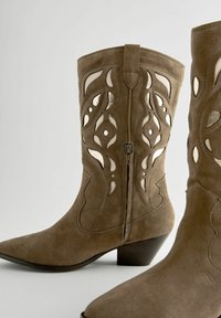 Bruna mockaläder cowboyboots med intrikata utskärningar, spetsiga tår, låg klack och en sidodragkedja för enkel påtagning.