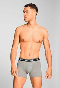 Shirtless man wearing grey Puma boxer briefs, standing against a plain light gray background, looking to his left.