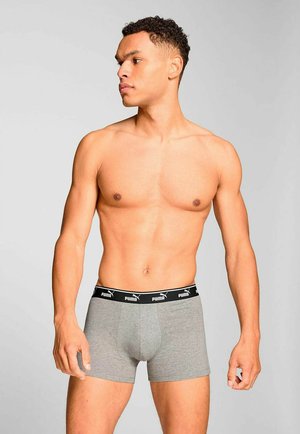 Shirtless man wearing grey Puma boxer briefs, standing against a plain light gray background, looking to his left.