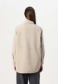 Beige kordfløyelskjorte med lange ermer, krage og rett bakstykk, med subtile vertikale striper og knappe mansjetter.