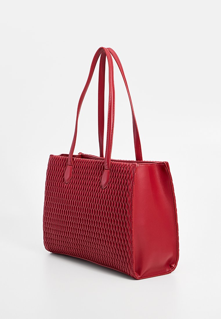 Sac fourre-tout synthétique rouge avec un motif texturé en nid d'abeille et des côtés lisses. Dispose de deux poignées robustes et d'une forme rectangulaire.