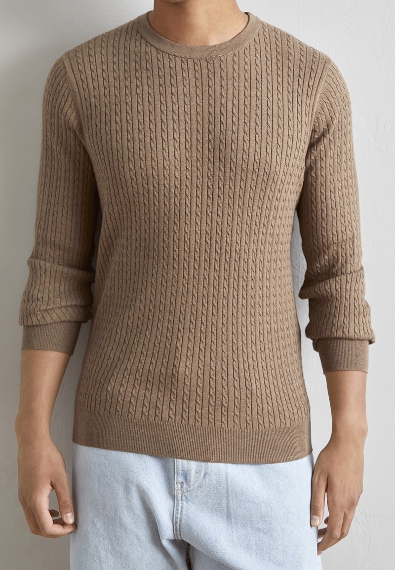 Brun stickad tröja med ett kabelmönster, rund halsringning och ribbade muddar och nederkant. Tillverkad av ett texturerat, mjukt material.