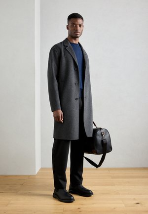 Grijze wol overjas met een notch lapel, geaccentueerd met zwarte knopen, gecombineerd met een blauwe trui, zwarte broek en een zwarte leren tas en laarzen.