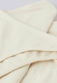 Ljusbeige tyg med en slät yta, med ett vikt mönster och synliga sömdetaljer längs kanterna. Mjukt och något skrynkligt.