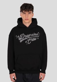 Hanorac negru cu glugă, cu inscripția „Dropsize Crew” în litere argintii sclipitoare. Are un buzunar frontal și manșete și tivuri striate.