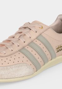 Μπεζ αθλητικό παπούτσι Adidas Japan με ανοιχτό γκρι ρίγες, διάτρητο δερμάτινο πάνω μέρος, μπεζ κορδόνια και υφασμένη μύτη.