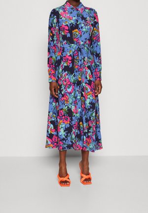 Florales Midikleid mit Kragen, lebhaft blauem Hintergrund, rosa und grünen Blumen sowie einer Taillenschleife. Kombiniert mit orangen Sandalen.