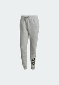 Szare dresy wykonane z miękkiego materiału, o zwężającym się kroju, z elastycznym paskiem w talii ze sznurkiem oraz dużym czarnym logo Adidas na jednej nogawce.