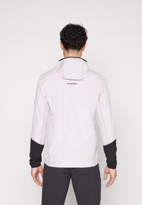 Φωτεινό ροζ μπουφάν με κουκούλα και μαύρες λεπτομέρειες, μακριά μανίκια και δομημένο μοτίβο. Λογότυπο μάρκας "MAMMUT" στην άνω πλάτη.