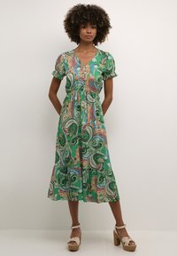 Green paisley dress featuring a V-neck, short puff sleeves, and a flowy skirt. Made from lightweight fabric, with colorful patterns and ruffled details.