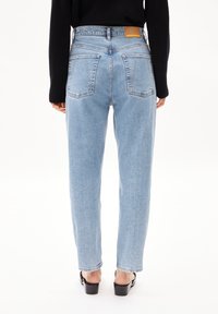 Des jeans taille haute bleu clair avec une coupe droite et deux poches arrière. Ils sont associés à un haut noir à manches longues et des chaussures à talons carrés.