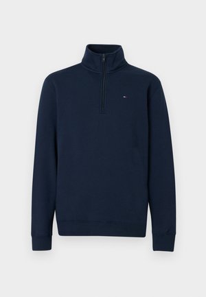 Marineblauwe fleece trui met een hoge kraag, halve ritssluiting en geribde manchetten. Voorzien van een klein logo op de borst. Gladde textuur.