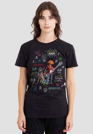 Schwarzes T-Shirt mit einem farbenfrohen Grafikdesign eines Jungen mit einer Gitarre und einem dekorierten Hund, umgeben von Text und dekorativen Elementen.