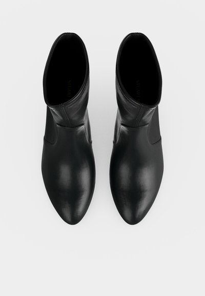Paire de bottines en cuir noir à bouts pointus, vues de dessus sur un fond clair uni.