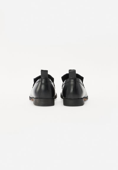 Mustad mustad nahast kingad sileda viimistluse, minimaalset disaini, madala kontsaga ja kangast aktsentidega säärelt. Tagantvaade, lihtne, kuid elegantne kuju.