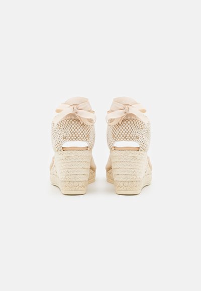Sandali con zeppa beige con tomaia in tessuto intrecciato, caratterizzati da dettagli a taglio e fiocchi sul retro. Tacco avvolto in juta per una maggiore texture.