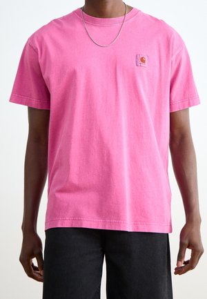 Homme portant un t-shirt Carhartt à manches courtes rose vif et un collier en chaîne argentée, assortis à un pantalon noir, vu du cou à la taille.