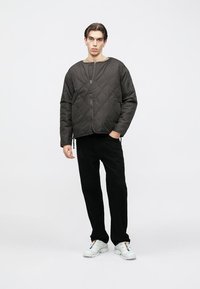 Õmmeldud must jakk ümarate kaelustega, esiküljel lukk ja elastsed detailid; kombinatsioonis mustade pükste ja valgete vabaajajalatsitega.