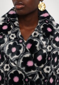 Cappotto in pelliccia sintetica con motivo floreale in tonalità di nero, bianco e rosa. Texture morbida con collo a scialle e distintive macchie rosa.