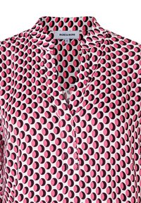 Kurzärmlige Bluse aus weißem Stoff mit einem Muster aus pinken und schwarzen Kreisen. Verfügt über einen V-Ausschnitt und eine lockere Passform. Markentag sichtbar.