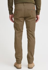 Chinos de algodón marrones con corte recto, dos bolsillos traseros con botones y una textura sutil, combinados con zapatos beige.