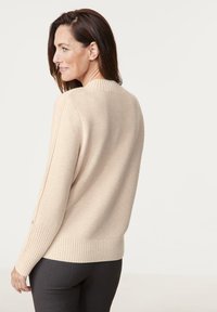 Beige Strickpullover mit geripptem Saum und Bündchen. Einfaches Design, etwas lockere Passform und runder Ausschnitt. Subtile Details an den Ärmeln.