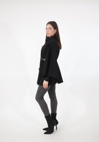 Sort kåbelignende frakke med brede ærmer, bæltet i taljen. Båret over en sort top og grå fitted jeans, kombineret med sorte spidse ankelstøvler.