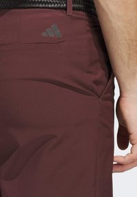 Bordo sportske hlače s glatkom teksturom, bočnom džepom i Adidas logom na stražnjem džepu.