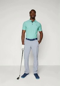 Γκολφ ενδυμασία που περιλαμβάνει ένα polo πουκάμισο σε μέντα πράσινο χρώμα, ανοιχτό γκρι παντελόνι και μπλε αθλητικά παπούτσια. Τα αξεσουάρ περιλαμβάνουν ένα γάντι και ένα γήπεδο γκολφ.