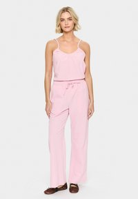 Pink, sleeveless, V-neck top paired with high-waisted, loose-fit, drawstring pants. Lightweight fabric with a smooth texture. Flat shoes.