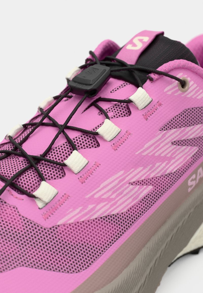 Lichte roze trailrunning schoen met een bovenwerk van mesh, elastische veters en een gestructureerde buitenzool voor grip. Opvallende merkgeving op de tong.