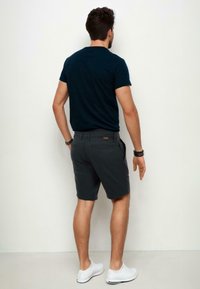 Navy blue short-sleeve t-shirt paired with dark gray shorts, featuring a pocket on the back. White sneakers complete the outfit.