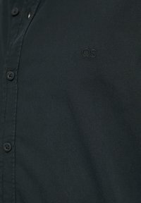 Camisa de botón de color verde oscuro hecha de una tela suave. Presenta un pequeño logo bordado "QS" cerca del pecho. Cuello clásico y cierre de botones estándar.