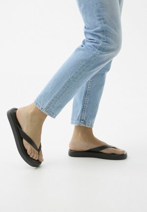 Sorte flip-flop sandaler med flad sål, med to brede stropper der krydser over foden. Båret med lyseblå cropped jeans.