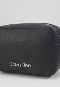 Černé kosmetické pouzdro z umělé kůže se stříbrným zipem a vytlačeným logem "Calvin Klein" na přední straně. Obdélníkový tvar s texturovaným povrchem.