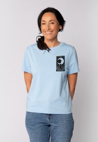 T-shirt en coton bleu clair à manches courtes, avec un imprimé graphique noir représentant une lune et des étoiles à l'avant.