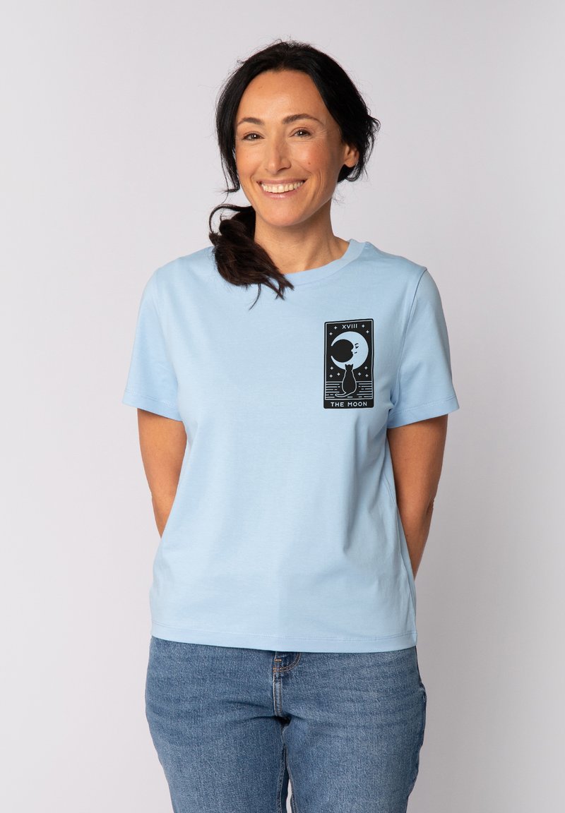 T-shirt en coton bleu clair à manches courtes, avec un imprimé graphique noir représentant une lune et des étoiles à l'avant.