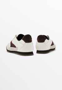 Sneakers a profilo basso in pelle bianca con accenti in suede viola scuro. Punta arrotondata, design con lacci e suola in gomma per una buona aderenza.