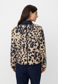 Giacca trapuntata beige con stampa animale blu, dotata di colletto in denim e superficie testurizzata. Vista posteriore con tasche laterali visibili.