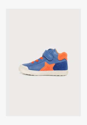 Παιδικό παπούτσι τύπου sneaker με μπλε και πορτοκαλί χρώμα, λουράκι με βέλκρο, πορτοκαλί σχεδιασμό αστεριού και λευκή λαστιχένια σόλα σε απλό φόντο.
