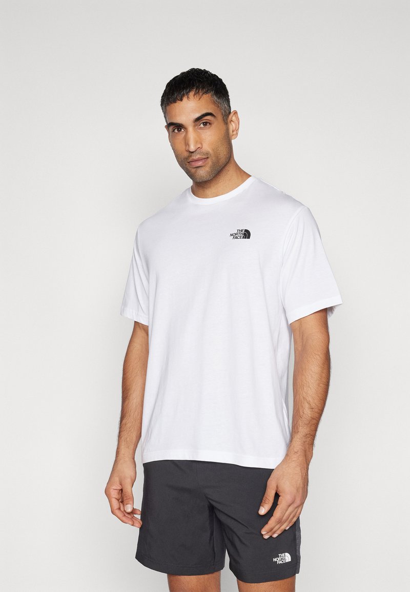 Camiseta de algodón blanca con cuello redondo y mangas cortas, que presenta un logo negro en el lado izquierdo del pecho. Textura de tejido suave.