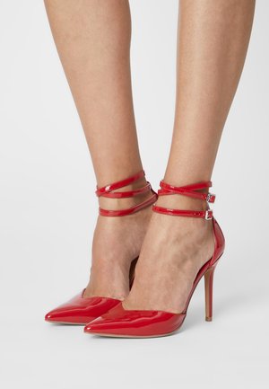 Escarpins en cuir verni rouge avec des bouts pointus et de fines brides autour de la cheville. Les chaussures présentent une finition brillante et un talon aiguille.