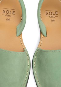 Green leather slip-on shoes with hand-stitched accents. Features a smooth texture, rounded shape, and branded insole with size 38.